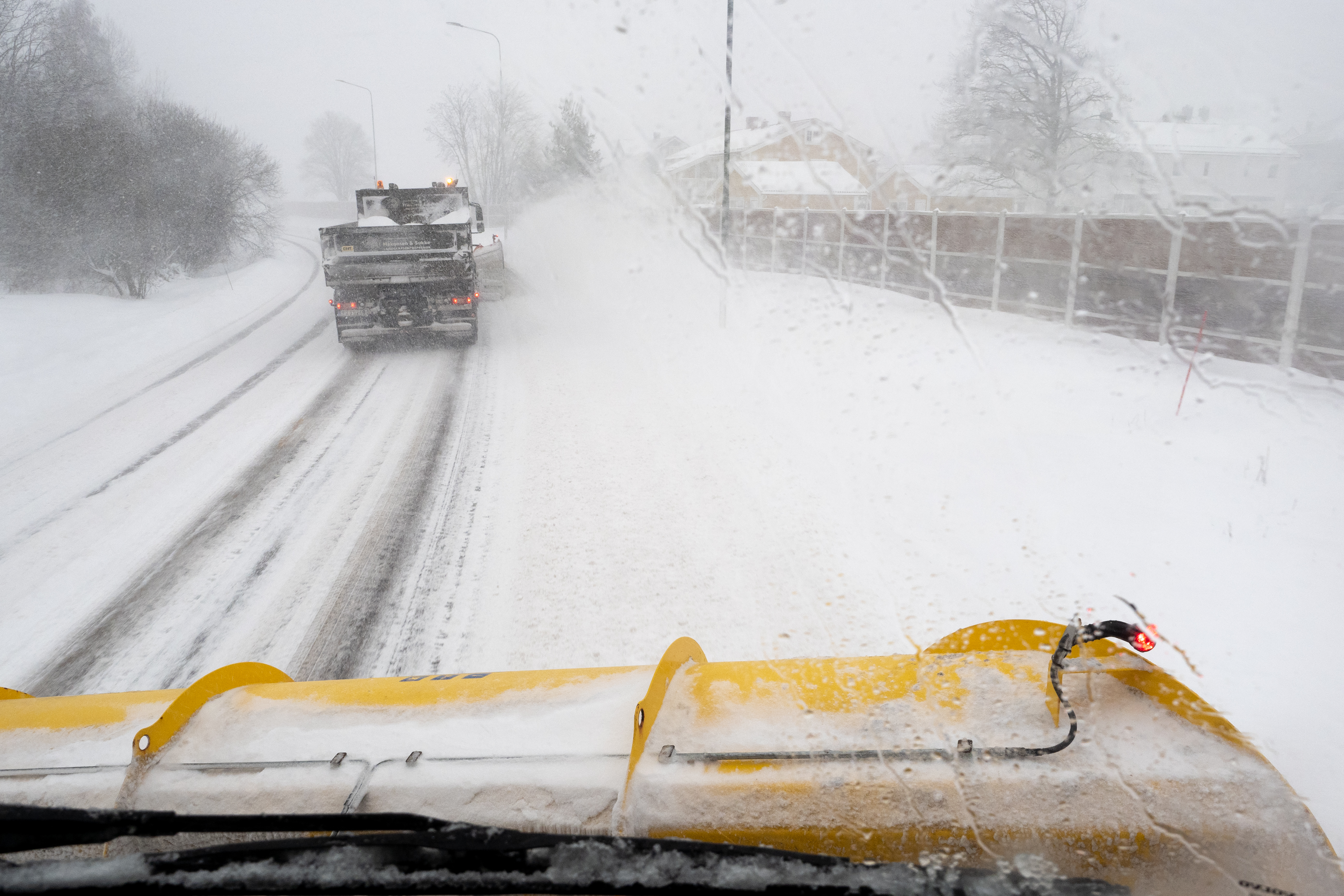 Fra førerhuset på en brøytebil som kjører bak en annen brøytebil i snøvær