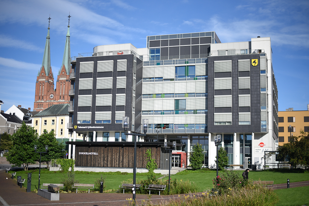 Stort bygg med Telemark fylkeskommunes logo og en park i forgrunnen