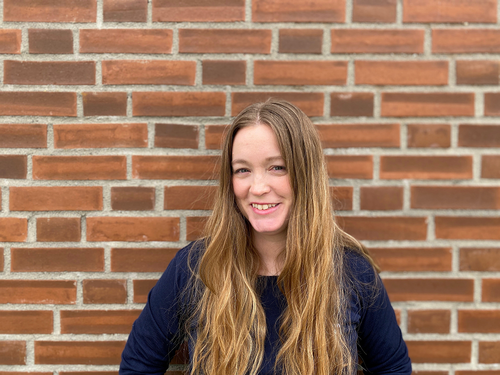 Kvinne som står smilende foran murvegg