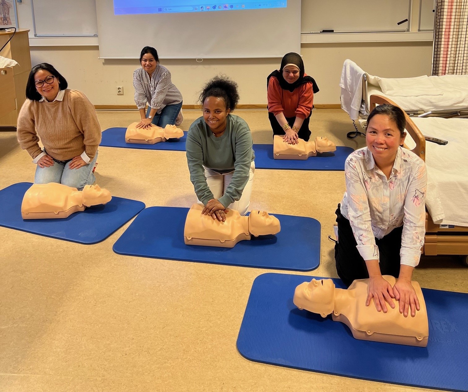 Elever sitter på gulv i klasserom og utfører hjertekompresjon på dukker