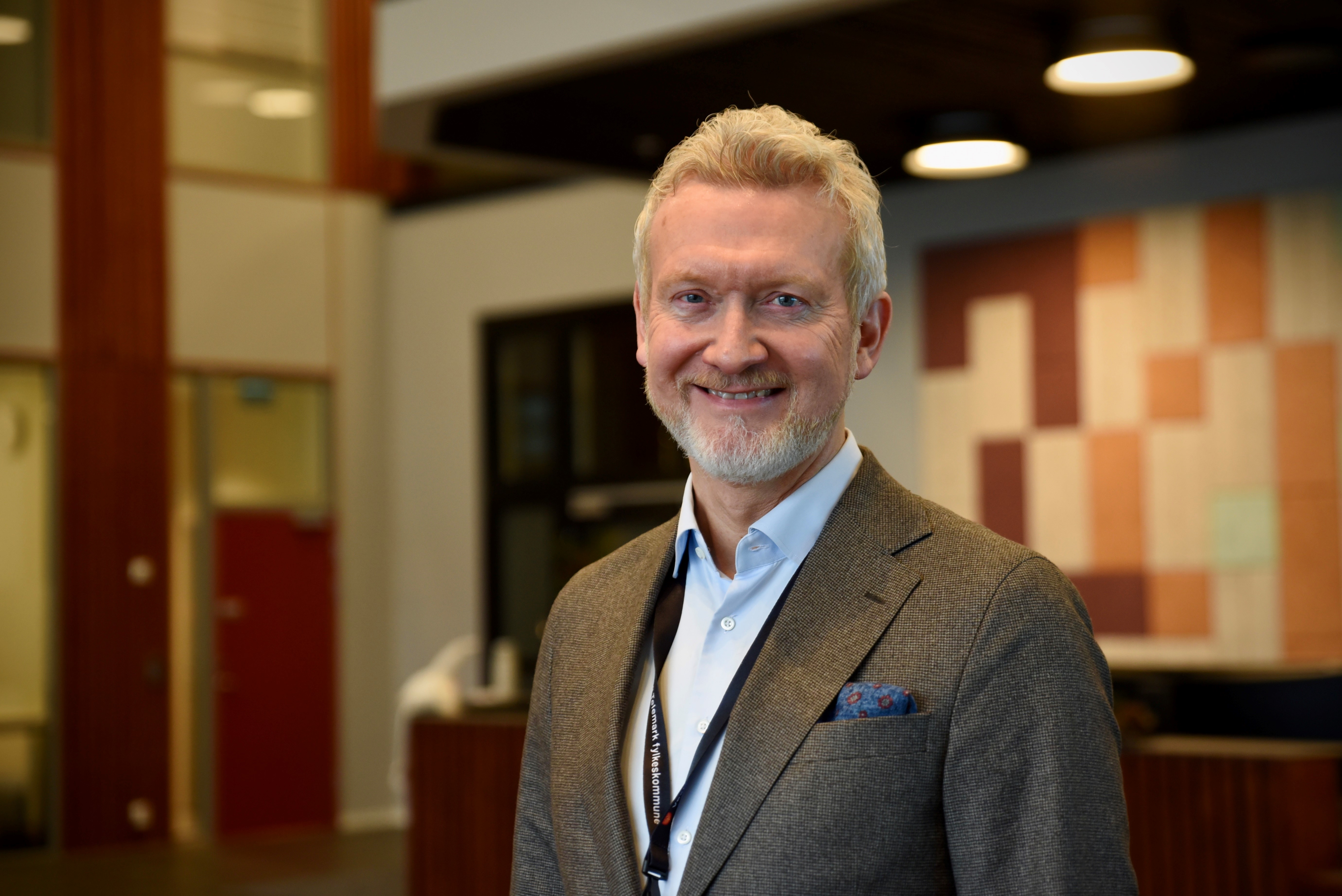 Mann i brun dressjakke og blå skjorte. Mannen har hvitt hår og skjegg.