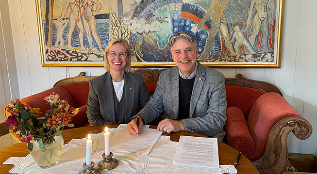 En mann og en kvinne sitter i en sofa. Mannen har papirer foran seg og en penn i hånd.