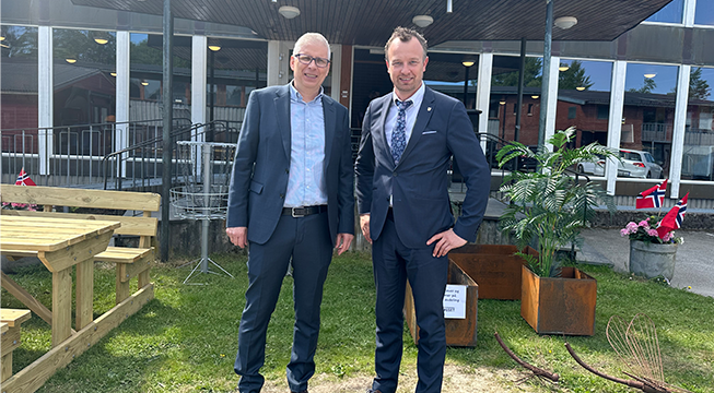 To menn i dress foran blomster og planter.