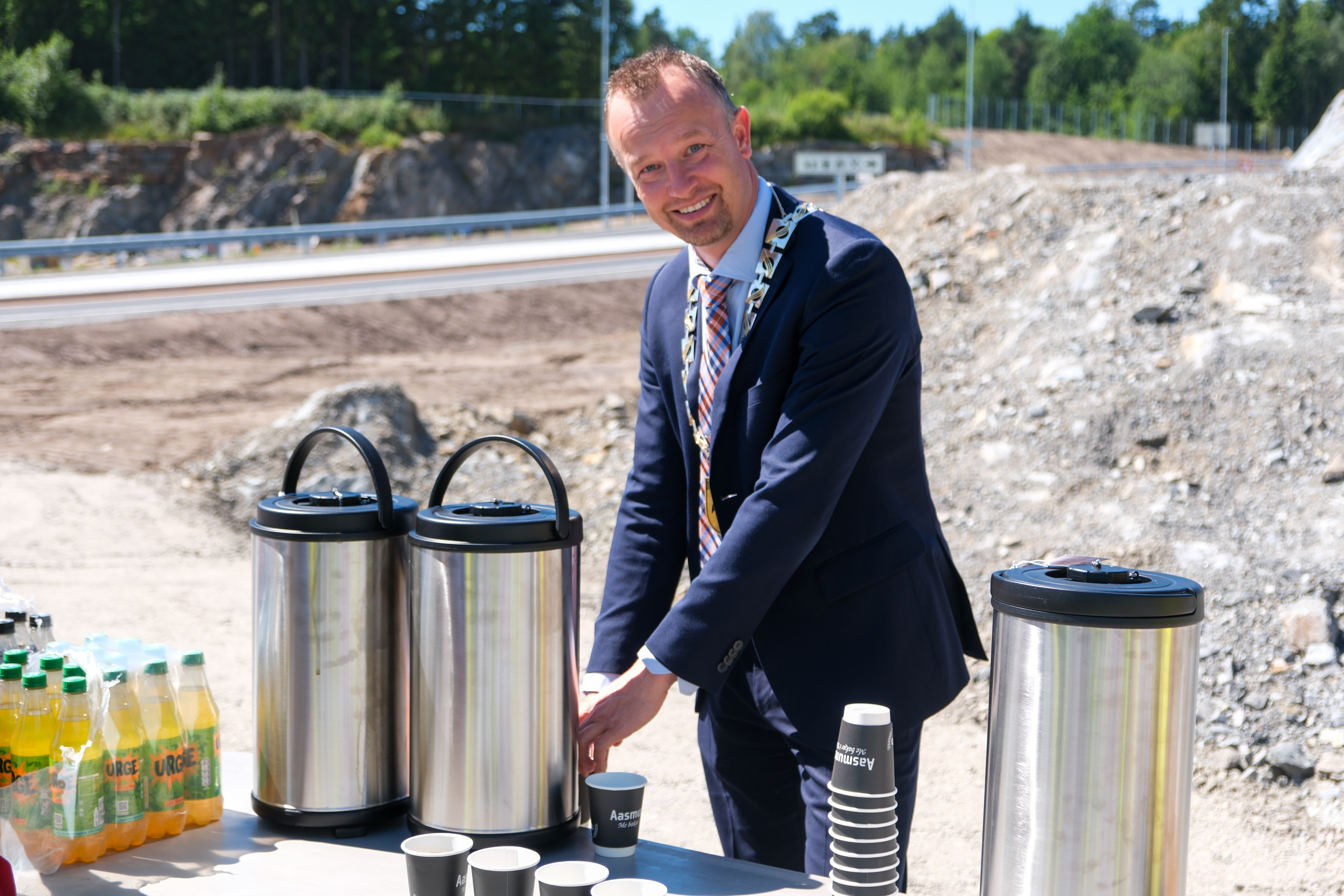 Fylkesordfører fyller bildets hoveddel, omgitt av kaffekanner og brusflasker