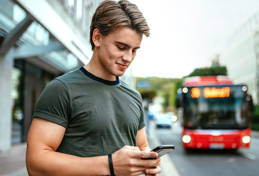 Ung mann ser på mobiltelefonen, mens en buss kjører i bakgrunnen