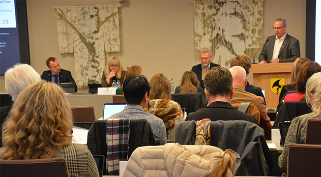 Mann står på en talerstol i en sal hvor det er mange mennesker