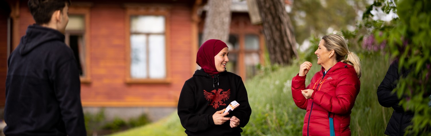 Bilde av kvinne med hijab som prater med hvit, middelaldrende kvinne.