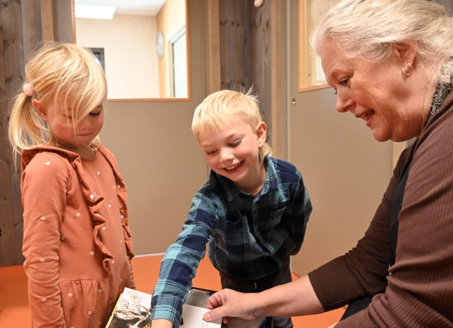 To barn og ei vaksen ser på ei bok i lag. Ungane er med på ordninga Tøyveskebibliotek. Foto: