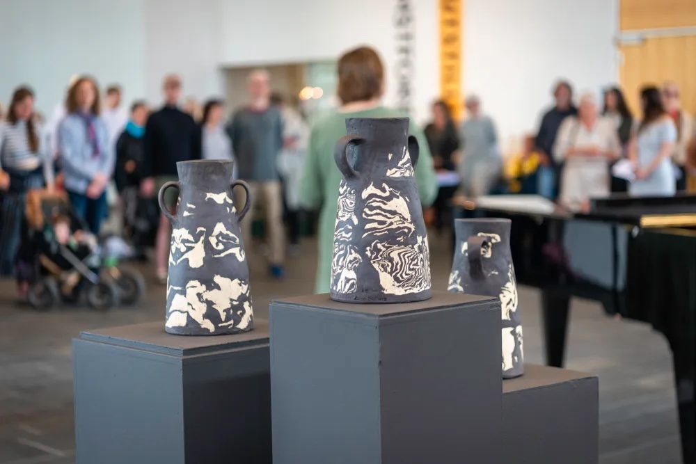 Tre svarte vaser med hvit utsmykning som står på noen rektangulære kasser.